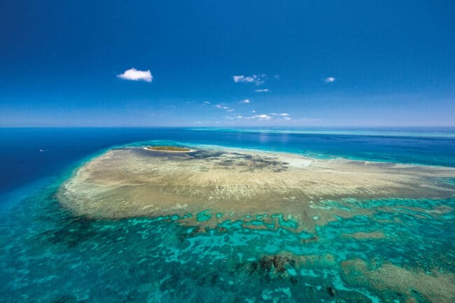 Aerial view of Green Island surrounded by coral reef and clear blue ocean on the Great Barrier Reef.