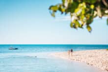 Couple walking along the shoreline of Green Island with turquoise water in the background.
