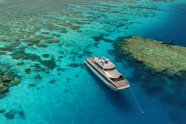 Silversonic dive boat floating above coral reef with snorkellers in crystal-clear blue water near Port Douglas.
