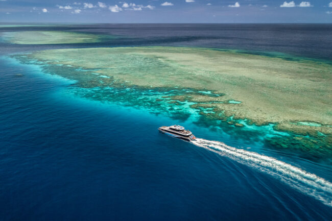 Silversonic high-speed catamaran cruising beside coral reefs under blue skies on the Great Barrier Reef.