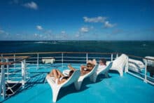 Guests relaxing on sun loungers on the top deck of Reef Encounter with reef views