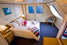 Large Top Deck stateroom on Reef Encounter with queen bed, ocean windows and colourful décor