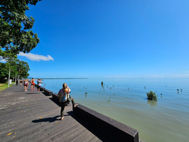 People standing and photographing the calm tropical water along the Cairns Esplanade.