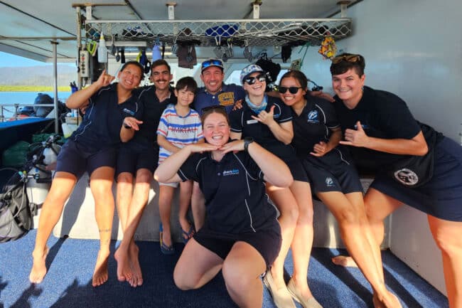 Smiling OceanQuest crew with a family guest group on the dive deck of the liveaboard.