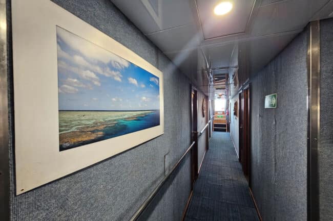 Hallway of OceanQuest liveaboard decorated with framed Great Barrier Reef photography.