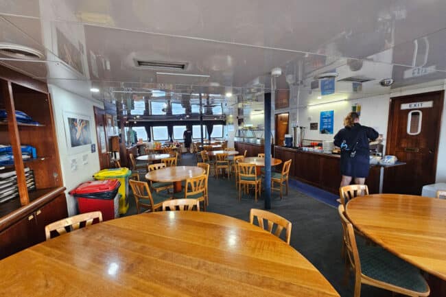 Crew member preparing meals inside the OceanQuest dining room with tables set for guests.