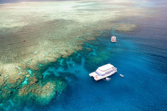 Aerial view of OceanQuest liveaboard on the Great Barrier Reef, surrounded by vivid blue and green coral shallows.