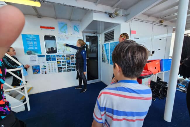 Dive instructor explaining reef maps and dive sites to guests aboard OceanQuest.