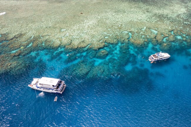 OceanQuest liveaboard moored at Norman Reef on the Great Barrier Reef, surrounded by turquoise coral lagoons.