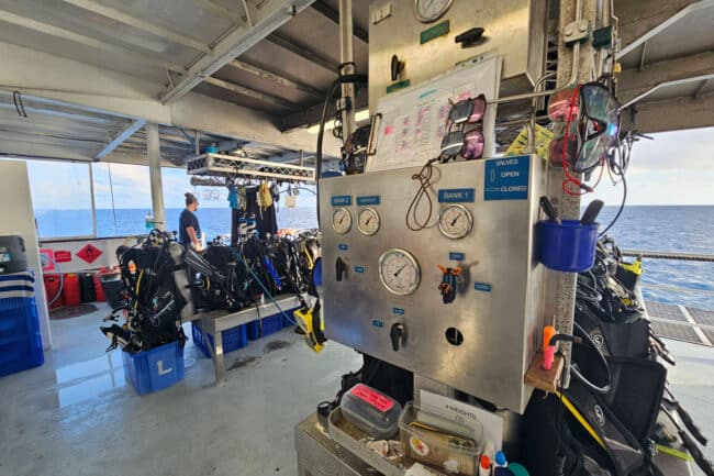 OceanQuest dive deck with scuba tanks, gear stations, and fill panel overlooking the Coral Sea.