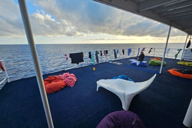 Upper sundeck on OceanQuest liveaboard with guests relaxing and drying towels in the morning sun.
