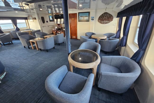 OceanQuest guest lounge with blue armchairs, tables, and wide ocean-view windows.
