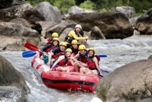 Rafting group navigating a rocky rapid with a guide steering down the Barron River in Cairns.