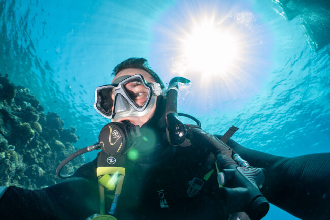 Scuba diver taking a selfie underwater in bright tropical sunlight on the Great Barrier Reef.