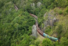 Kuranda Scenic Railway train curving through dense rainforest and rocky cliffs in Barron Gorge