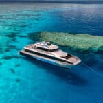 Silversonic high-speed aluminium catamaran anchored over vibrant coral reefs on the Great Barrier Reef near Port Douglas, with snorkellers exploring the Agincourt Ribbon Reefs.