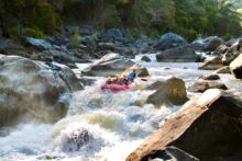 Rafting group powering through a rapid on the Barron River surrounded by rocky canyon scenery.