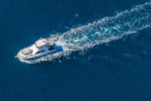 Aerial view of a private luxury yacht cruising across deep blue ocean off Cairns, leaving a white wake on the Great Barrier Reef.