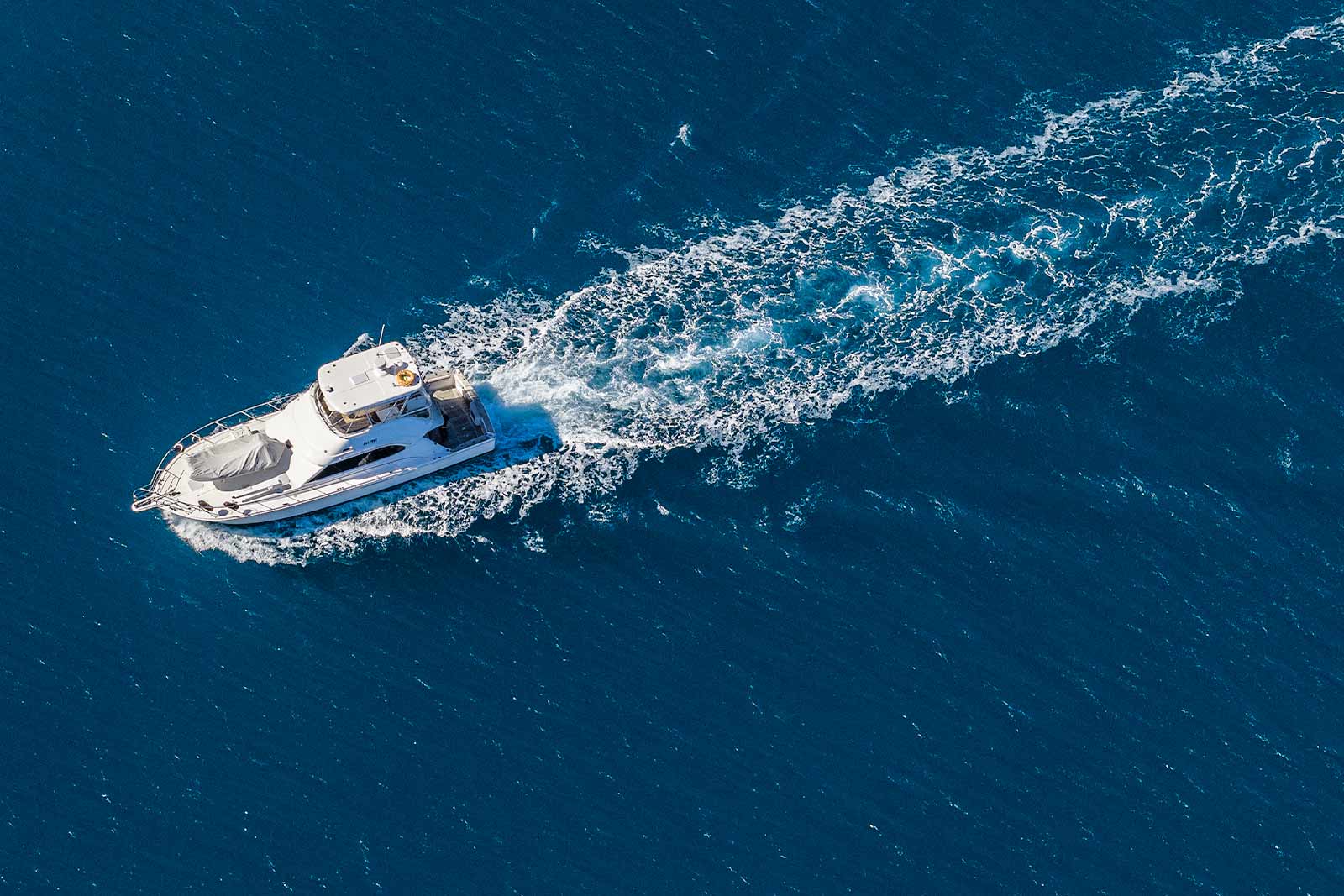 Aerial view of a private luxury yacht cruising across deep blue ocean off Cairns, leaving a white wake on the Great Barrier Reef.